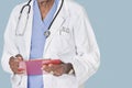 Midsection of male doctor writing on clipboard over light blue background Royalty Free Stock Photo