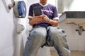 Man using smartphone while sitting on toilet bowl at home Royalty Free Stock Photo