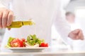 Midsection of mature chef using pouring oil on salad in plate at restaurant