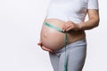 Midsection of pregnant woman measuring her belly with a tape to keep track of her fetus development, white background