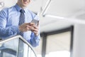 Midsection of smiling businessman using smartphone while standing at office Royalty Free Stock Photo