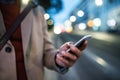 Midsection view of businessman with smartphone standing on a street in the evening.