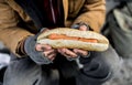 A midsection view of homeless beggar man outdoors in city, holding hot-dog.