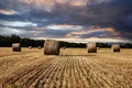 Field with hay bales under stormy sky and rays of light Royalty Free Stock Photo