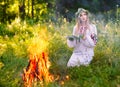 Midsummer. Woman weaving a wreath near the fire.