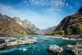 Mighty mountain river flows along stony banks among rocky mountains against a clear blue sky. Turquoise water of stormy river and