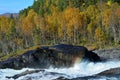 Mighty waterfall in autumn with colorful forest and small rainbow created by water vapor