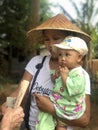 Migun, Myanmar - November 7, 2019: Burmese woman wearing asian conical hat an carrying her child