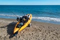 Orange sea kayak with fishing equipment and a caught fish on Cala de Mijas beach.