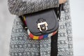 Woman poses for photographers with black and colorful leather bag and intricate design gray coat, before
