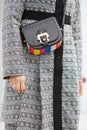 Woman poses for photographers with black and colorful leather bag and intricate design gray coat, before