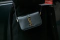 Woman poses for photographers with Yves Saint Laurent black leather bag with golden logo before Etro and