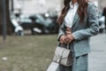 Street style, woman wearing white cropped shirt, a gray blazer jacket, gray matching suit pants, a beige leather handbag and