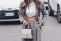 Street style, woman wearing white cropped shirt, a gray blazer jacket, gray matching suit pants, a beige leather handbag and