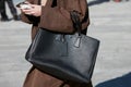 Woman with black leather Prada bag and brown trench coat before Marco Rambaldi fashion show,