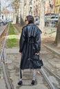 MILAN, ITALY - FEBRUARY 25, 2023: Woman with black leather trench coat with Missguided writing and black Yves Saint Laurent bag