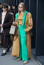 MILAN, ITALY - FEBRUARY 24, 2023: Woman with green Adidas trousers and jacket and beige trench coat before Gucci fashion show,