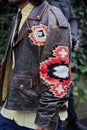 Man with brown leather jacket with red, white and black decorations before Magliano fashion show