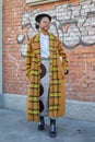 Woman with beige and yellow checkered coat and black hat before Fendi fashion show, Milan Fashion