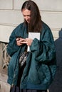 Woman with blue bomber jacket looking at smartphone before Salvatore Ferragamo fashion show,
