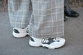 Woman with white and black New Balance sneakers and gray checkered trousers before Emporio Armani