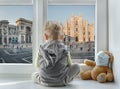 Milan/Italy - March 05, 2020: Child in home quarantine looking out of the window with his sick teddy bear at Milan Cathedral