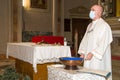 Priest with protective mask against Covid-19, celebrates mass in front of the baptismal font