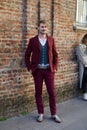 Man with burgundy jacket and trousers and Gucci belt and sneakers before Salvatore Ferragamo