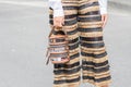 Model wears a pair of golden and black stripes trousers as well as an original semi-transparent handbag
