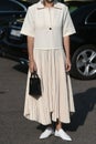 Street style outfit, fashionable woman wearing creme white polo, pleater skirt, black bag on