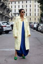 Tamu McPherson with pale yellow, long coat, electric blue dress and green pointed shoes before