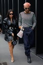 Woman with black shiny jacket and man with pink hair walking before Gucci fashion show, Milan