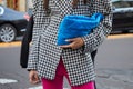 Woman with black and white houndstooth jacket, blue bag and pink trousers before Bottega Veneta