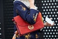 Woman with red Gucci suede bag with golden logo and blue jacket with floral design before Gucci