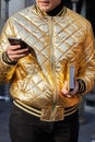 Man with golden bomber jacket looking at smartphone before Daks fashion show, Milan Fashion Week street style