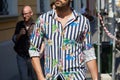 Man with white and blue striped shirt with floral decorations before Prada fashion show, Milan Fashion Week