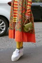 Woman with green Furla bag, orange and yellow jacket and white wedge heel shoes before Antonio Marras