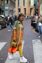 Woman with orange, green, yellow clothing and white wedge heel shoes before Antonio Marras fashion show,