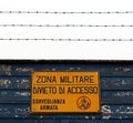 Military area with yellow sign: `Zona militare, divieto di accesso, sorveglianza armata`. Translation: `Milita