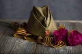 Military cap, carnations, Saint George ribbon on a wooden surface