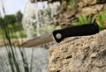 Folding knife stainless steel sharp blade black handle close up still life stone background