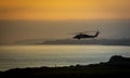 A military helicopter flying toward the left in a cloudy sunset