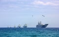 Military helicopters and military planes fly over the combat liners on the coast