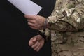 A military man in a camouflage uniform is handcuffed on a black background, with a white sheet of paper in his hand. Concept: mili