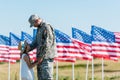 Military man looking at cute child in straw hat near american flags with stars and stripes