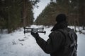 A military man with a rifle behind his back launches a drone in the forest in winter. Close up Royalty Free Stock Photo