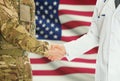 Military man in uniform and doctor shaking hands with national flag on background - United States