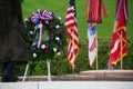 Military servicemember placing a floral wreath in front of a display of multiple flags