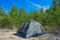 A military tent in an evergreen forest. Tourist and hiker layover on white sand in a small camouflage tent