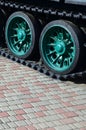 A military vehicle on caterpillar tracks stands on a square of paving stones. Photo of green caterpillars with metal wheels that